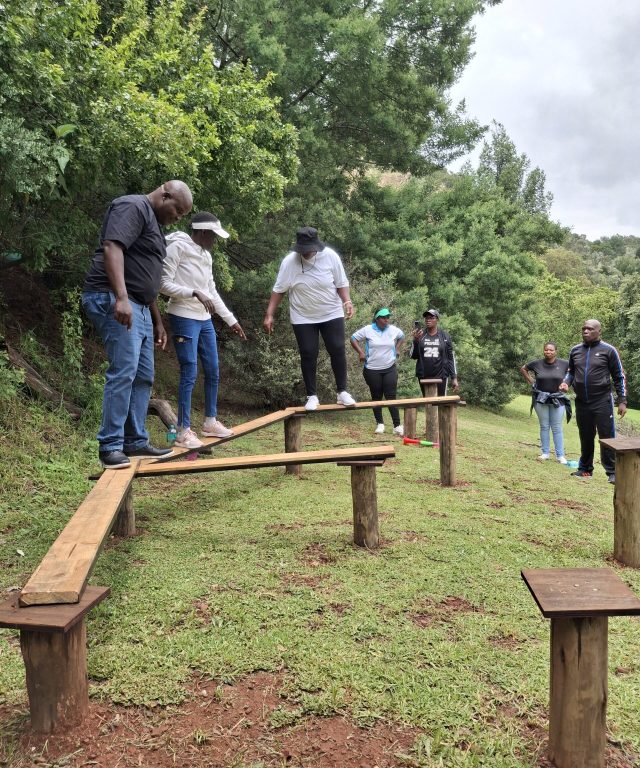 School leadership participants crossing stepping stones during a team building challenge that develops communication, trust, and problem-solving skills.
